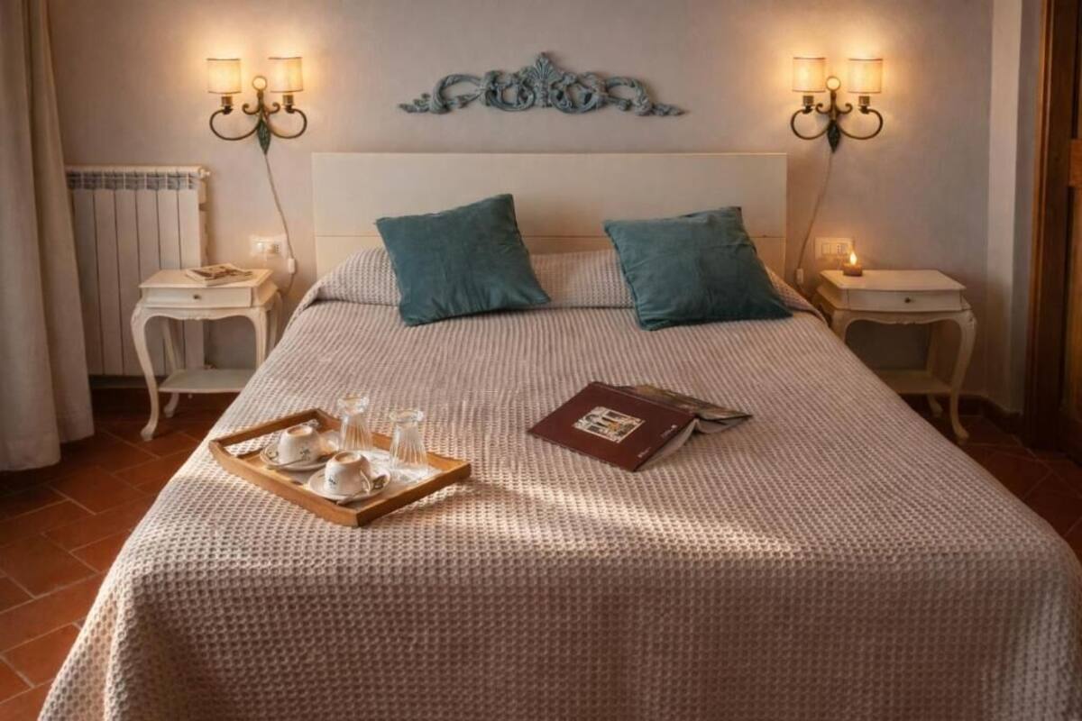 Un lit bien fait, avec un plateau contenant du thé et un livre, deux tables de chevet avec des lampes et un radiateur.