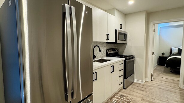 A compact kitchen with a stainless steel refrigerator, microwave, and stove, white cabinets, and a wooden floor. - Newly constructed apartment located near Canada’s Wonderland, Vaughan Mills Mall (Vaughan)