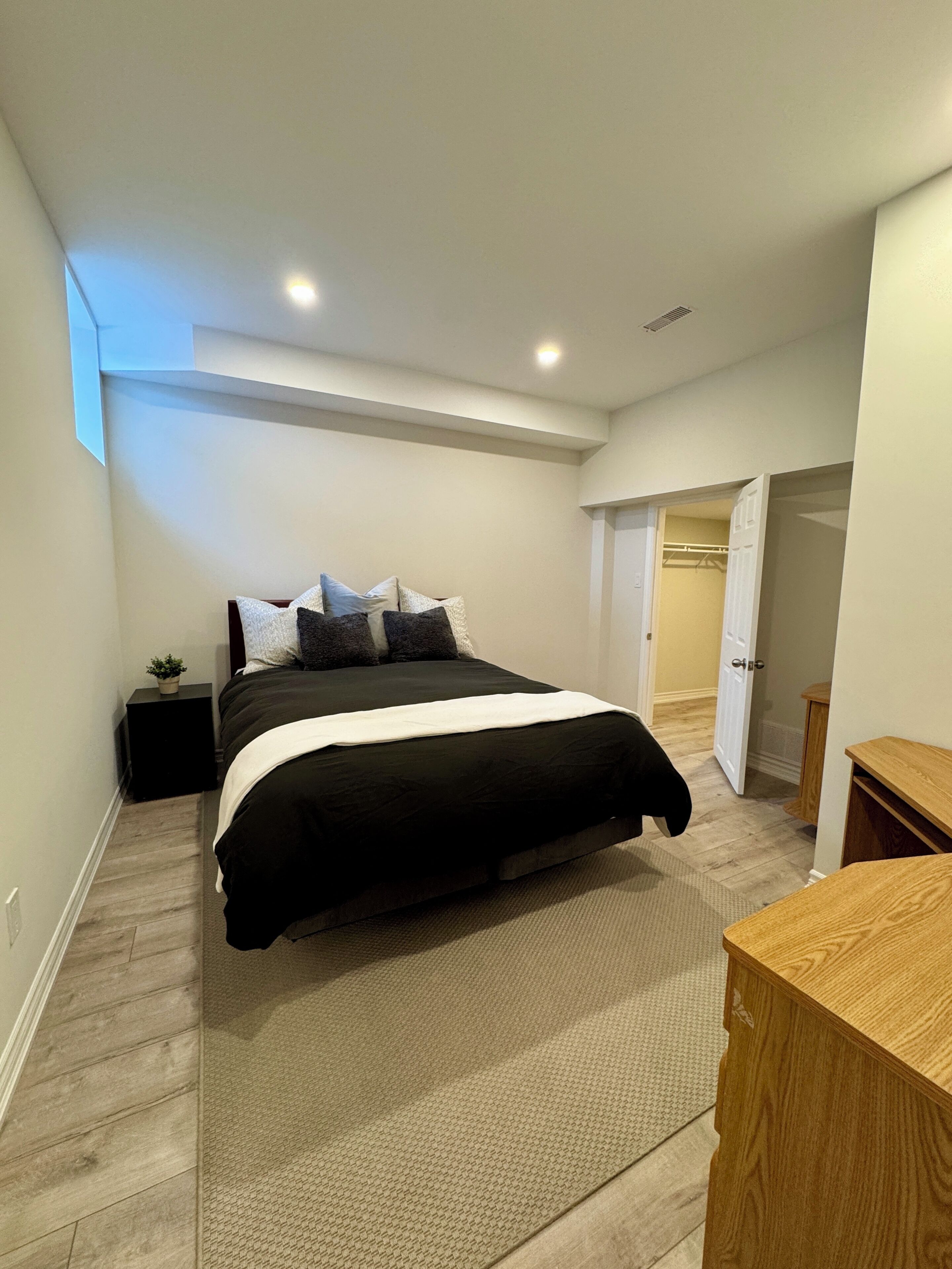 Un dormitorio con una cama, mesitas de noche, una planta pequeña y un banco de madera.