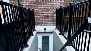 A staircase with black railings leading to a white door, set against a brick wall. - Newly constructed apartment located near Canada’s Wonderland, Vaughan Mills Mall (Vaughan)