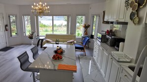 A modern kitchen with a central island, dining area, and large windows offering a view of the outdoors. - New 3BR Guest Suite |  Lakeview,  Private Entry (Kelowna)