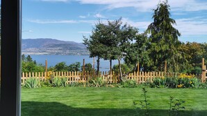 A view of a lake with mountains in the background, a wooden fence, and various plants in the foreground. - New 3BR Guest Suite |  Lakeview,  Private Entry (Kelowna)