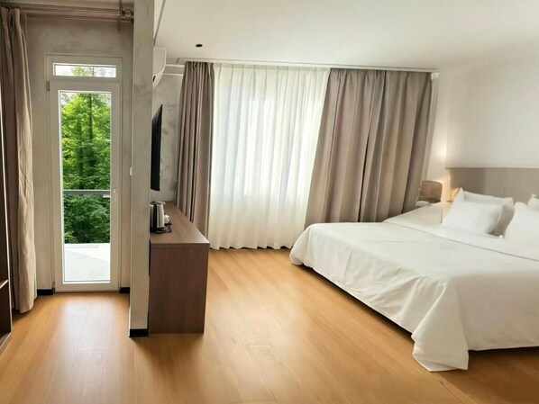 A hotel room with a bed, a desk, a television, and a view of greenery through the window. - Sky Vista Hotel (Belgrade)