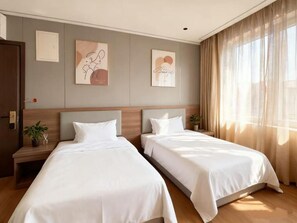 A hotel room with two beds, a wooden headboard, a nightstand with a plant, and artwork on the wall.