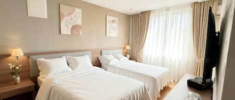 A hotel room with two beds, a desk, a TV, and a window with curtains.