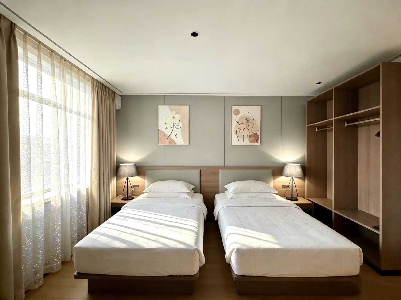 A hotel room with two beds, a wardrobe, and artwork on the walls.