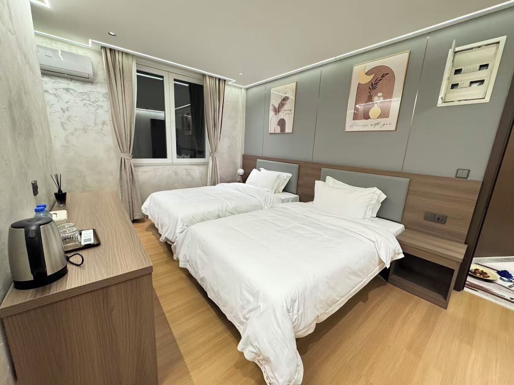 A hotel room with two beds, a desk with a coffee maker, a window with curtains, and wall art.