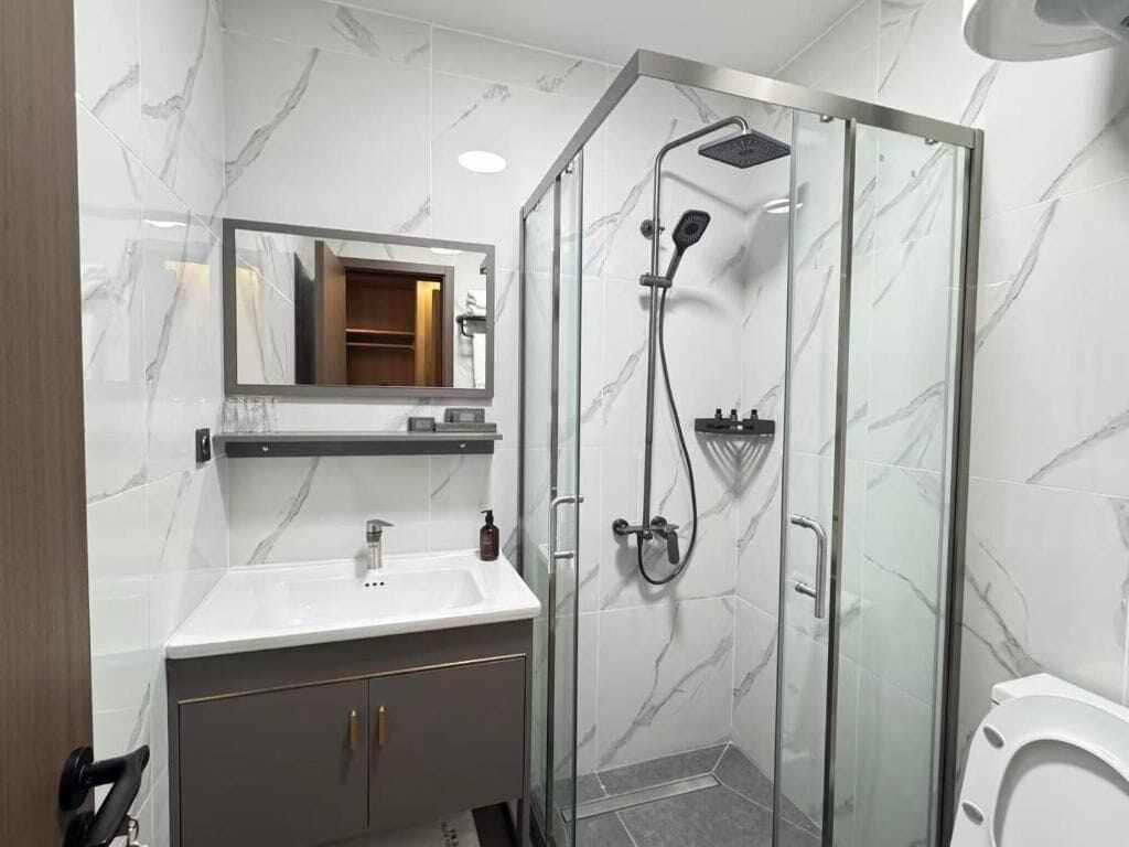 Un baño con ducha de vidrio, un lavabo blanco y un espejo sobre el tocador.