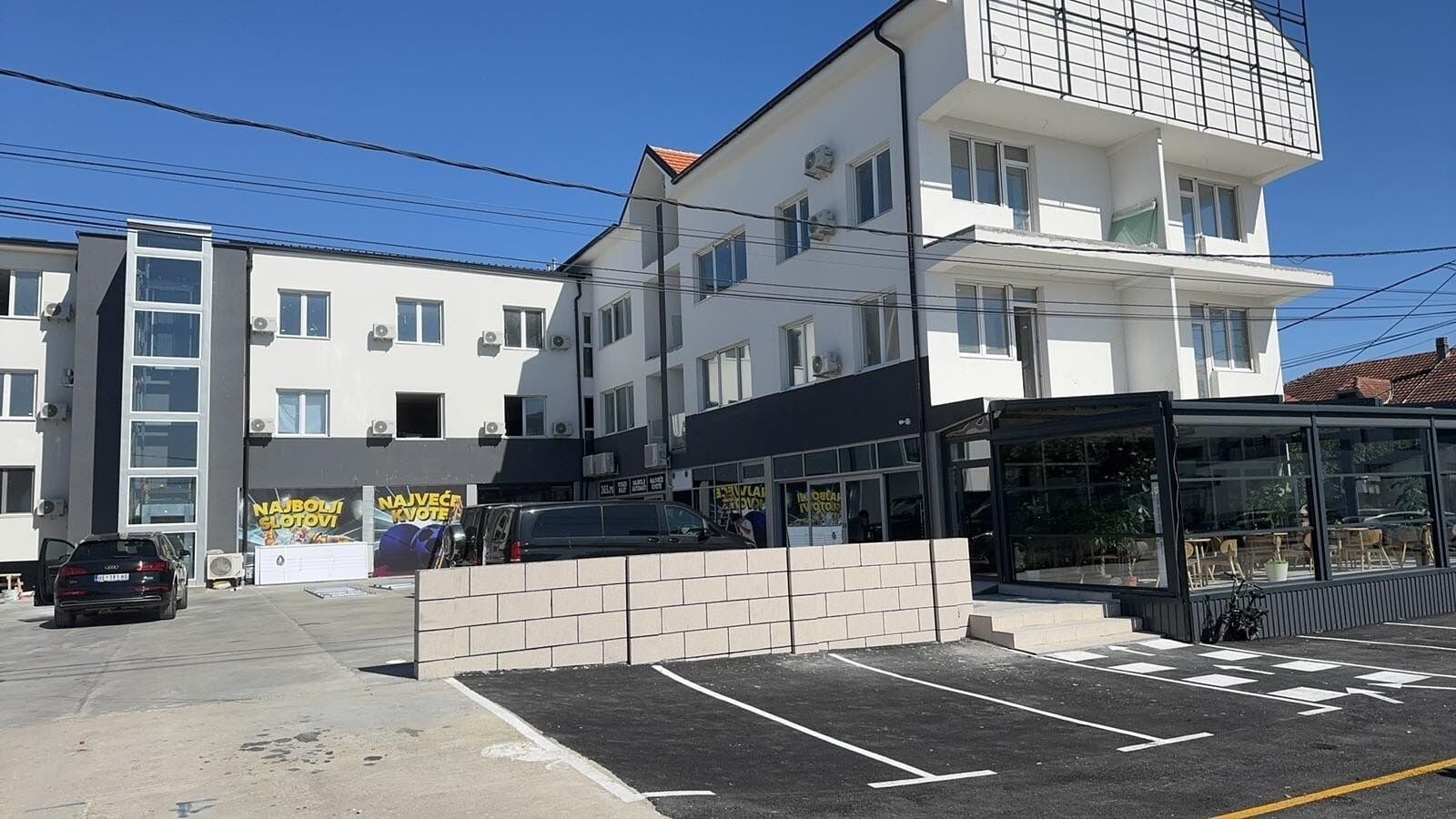 A multi-story building with a parking area, a glass entrance, and a signboard.