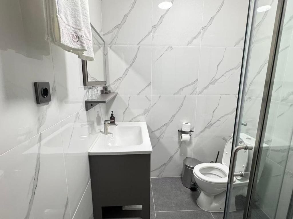 A modern bathroom with a marble backsplash, a sink, a toilet, and a glass shower enclosure.