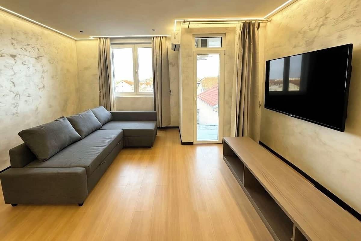 Un saló modern amb un sofà modular, una televisió de pantalla plana i una porta corredissa de vidre que dona a una zona exterior.