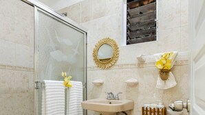A bathroom with a glass shower enclosure, a sink, a toilet, and a small window with a decorative mirror. - Cozy Apartment Rental in Puerto Plata, Dominican Republic (Puerto Plata)