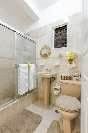 A bathroom with a glass shower enclosure, a sink, a toilet, and a small window with a decorative mirror. - Cozy Apartment Rental in Puerto Plata, Dominican Republic (Puerto Plata)