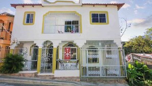 A two-story building with a white facade, yellow trim, and barred windows. - Cozy Apartment Rental in Puerto Plata, Dominican Republic (Puerto Plata)