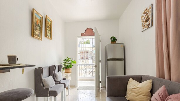 A modern living room with a sofa, a dining table, and chairs. There is a refrigerator and a potted plant on the wall. - Cozy Apartment Rental in Puerto Plata, Dominican Republic (Puerto Plata)