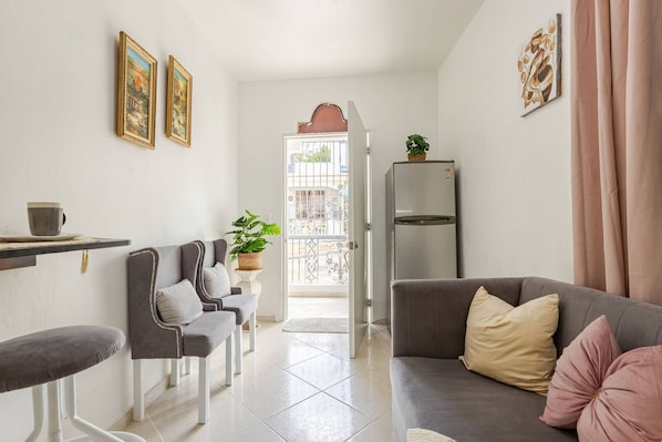 A modern living room with a sofa, a dining table, and chairs. There is a refrigerator and a potted plant on the wall. - Cozy Apartment Rental in Puerto Plata, Dominican Republic (Puerto Plata)