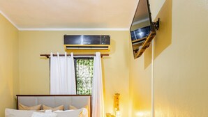 A hotel room with a bed, a TV mounted on the wall, a bedside table, and a window with curtains. - Cozy Apartment Rental in Puerto Plata, Dominican Republic (Puerto Plata)