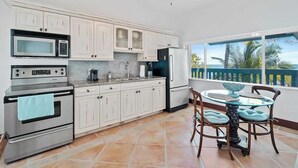 Een keuken met witte kasten, roestvrijstalen apparatuur, een eettafel met stoelen en uitzicht op zee.