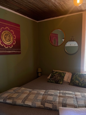 Une chambre à coucher avec un lit, des oreillers, un miroir fixé au mur et un objet décoratif.