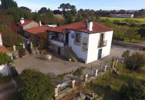 Ein weißes Gebäude mit rotem Ziegeldach, einem kleinen Balkon und einem gepflasterten Innenhof mit Gartenmöbeln.