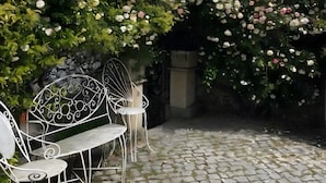 A garden with a white metal bench and a white metal chair, surrounded by a hedge of pink and white flowers.
