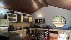 A compact kitchen with modern appliances, a dining area with a glass table, and a large window offering a view of trees.