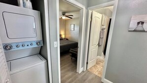 Een wasserij met gestapelde wasmachine en droger, een plafondventilator en een gang naar een slaapkamer.