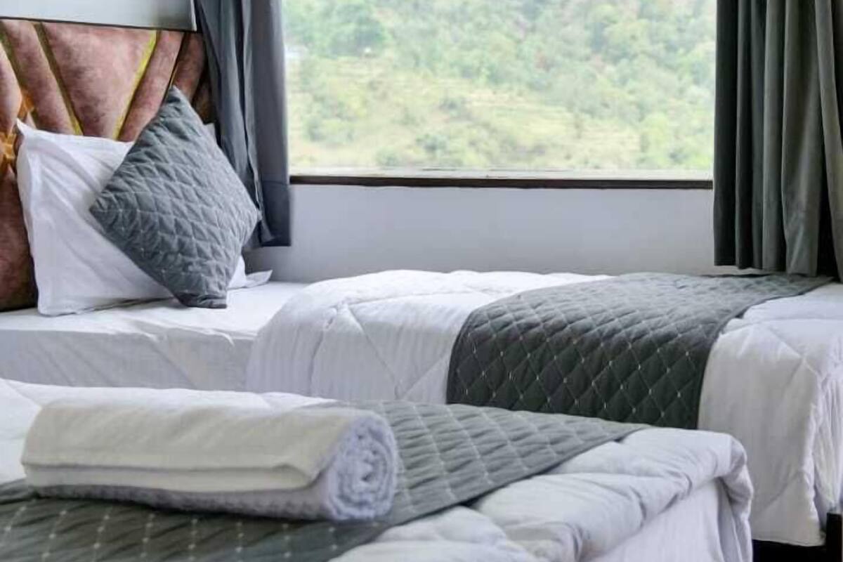 Un dormitorio con dos camas, una ventana con cortinas y vistas a un paisaje montañoso.