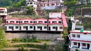A multi-story building with a red roof, surrounded by greenery and other buildings. - Ayu Hotels  (Ukhimath)