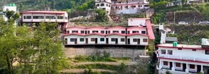 A multi-story building with a red roof, surrounded by greenery and other buildings. - Ayu Hotels  (Ukhimath)