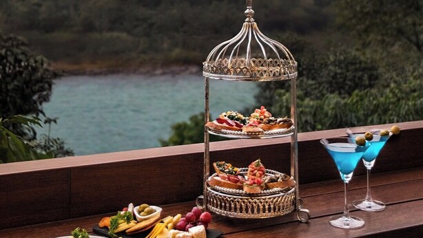 A balcony with a tiered dessert stand, a martini glass, and a plate of cheese and crackers. - Ayu Hotels  (Ukhimath)
