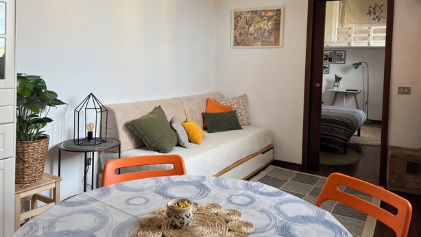 Een gezellige kamer met een bank, een eettafel en een klein bijzettafeltje met een lamp.