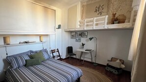 Een slaapkamer met een bed, een bureau, een stoel, een lamp en een raam met uitzicht op bomen.