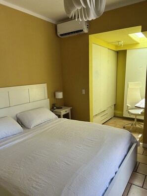 A hotel room with a bed, bedside table, lamp, and a corner with a chair and desk. - BEACHSIDE OCEAN PARK TROPICAL GARDEN STUDIO WITH PATIO     High-Speed WiFi (San Juan)
