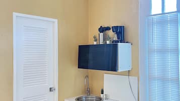 A compact kitchen with a sink, a small refrigerator, and a window with blinds.