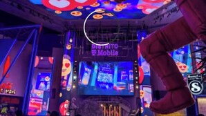 Un espacio interior concurrido con letreros de neón y pantallas digitales, incluyendo una que dice 'DISTRITO DE MOBILE'.