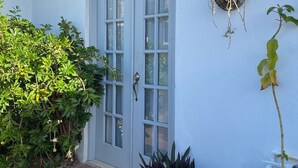 Un edificio blanco con techo de tejas, puerta con paneles de vidrio y una maceta colgante con planta.