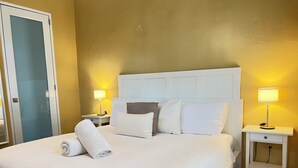 Una cama bien hecha con sábanas blancas, un cabecero blanco y dos lámparas de noche.