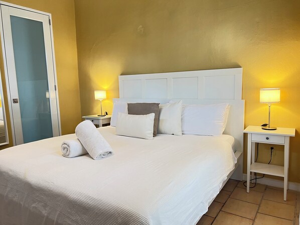A neatly made bed with white linens, a white headboard, and two bedside lamps. - BEACHSIDE OCEAN PARK TROPICAL GARDEN STUDIO WITH PATIO (San Juan)