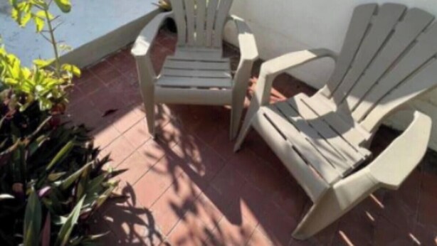Un patio con dos sillas Adirondack, una planta en maceta y piso de baldosas.