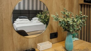 Pared de madera con un espejo redondo que refleja una cama, un control remoto, una cesta blanca y un florero con plantas verdes.
