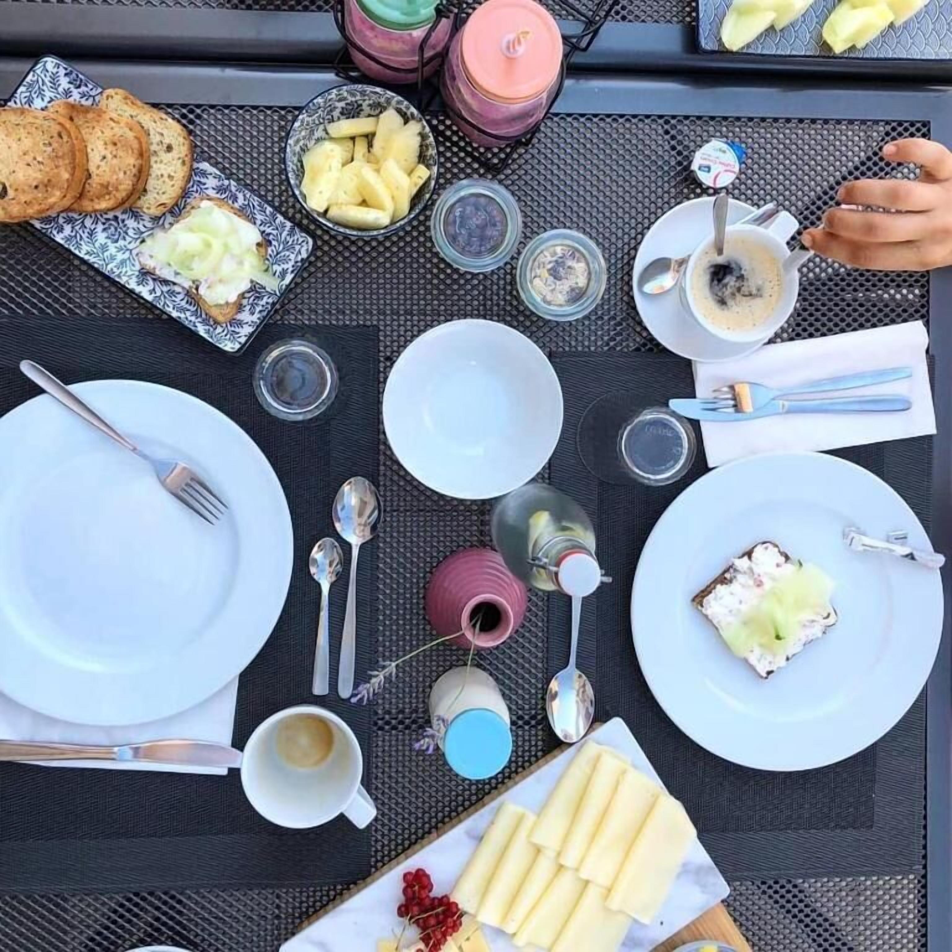 A table set for breakfast with plates, cutlery, and a variety of food items.