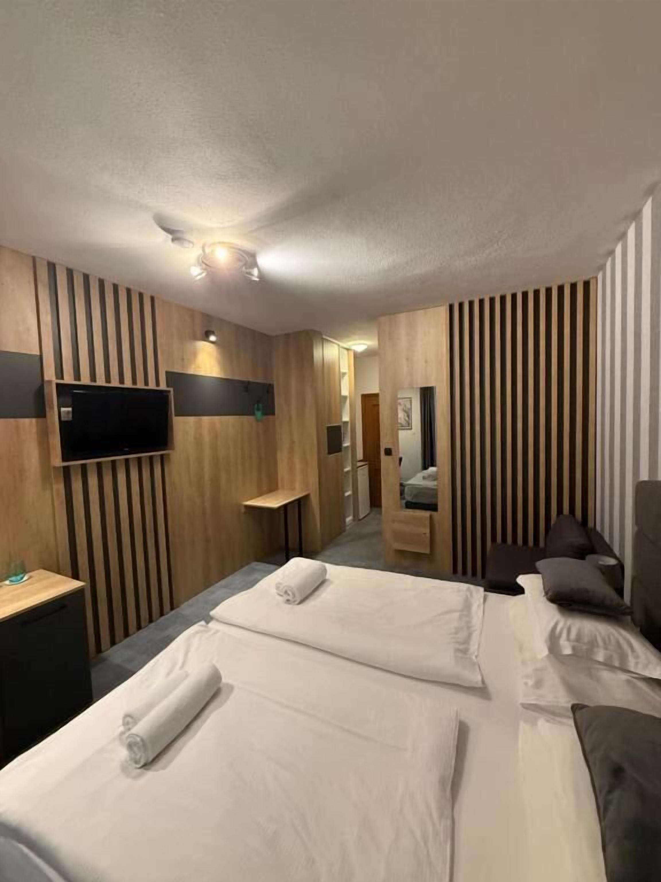 A hotel room with two beds, a TV mounted on the wall, a desk, and a mirror.