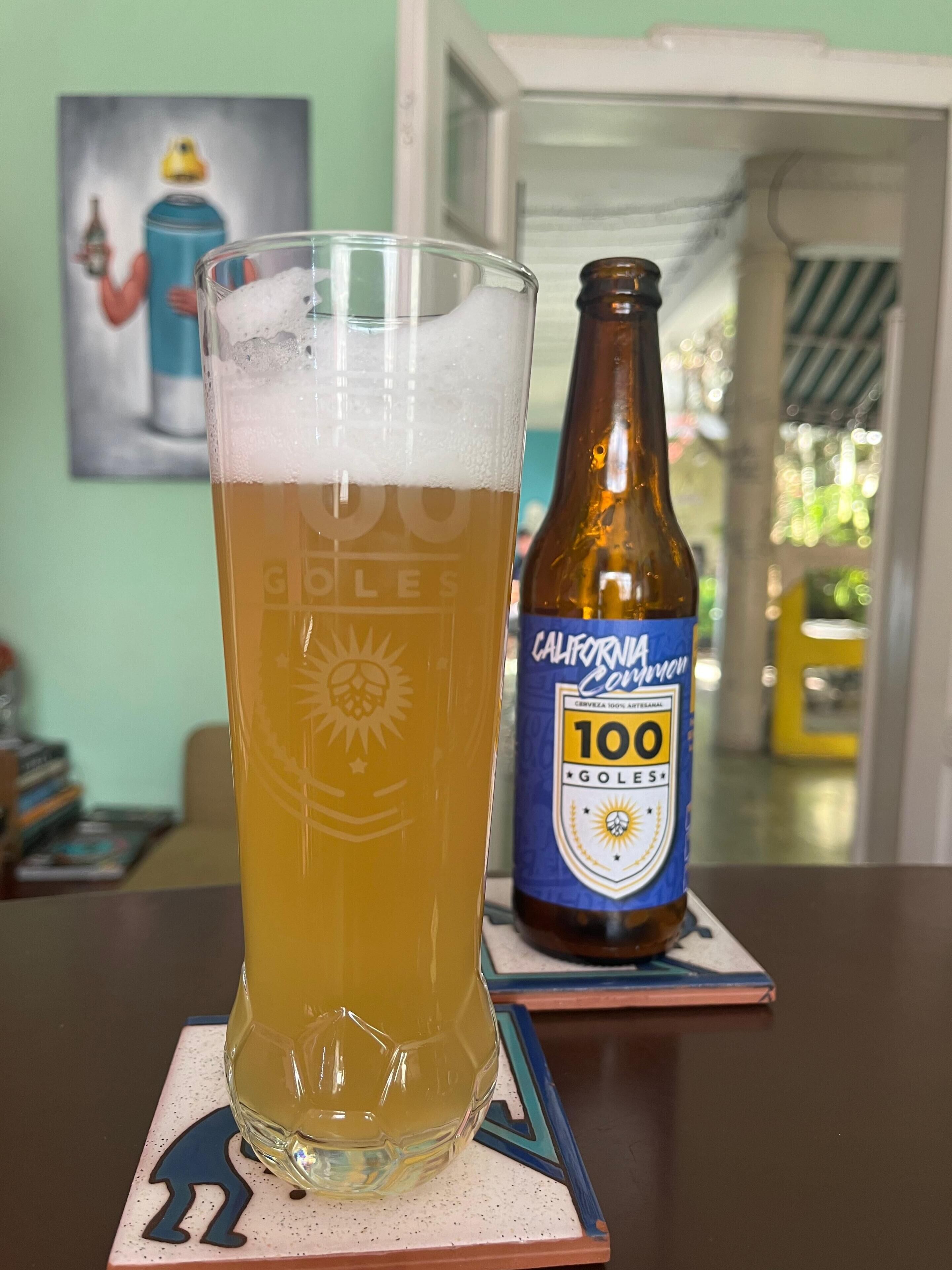 A glass of beer on a coaster with a bottle of California 100 next to it.