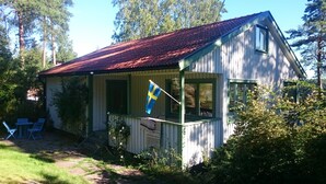 Eine kleine Holzhütte mit rotem Dach, einer Flagge und einer Veranda mit Stühlen.
