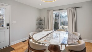 Un coin repas comprenant une table ronde, six chaises, une étagère en métal et une fenêtre avec des rideaux.