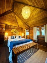 Interior de una cabaña de madera con cama, banco y lámpara colgante.