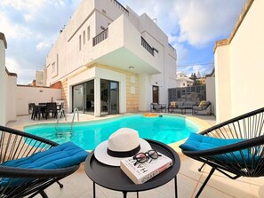 A modern poolside area with a pool, lounge chairs, and a dining table.