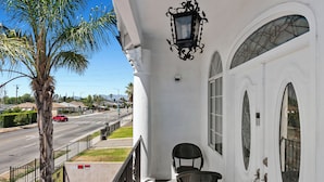Un edificio blanco con balcón, una palmera y vista a la calle.