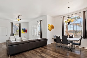 A spacious living area with a sofa, dining table, chairs, and a chandelier.
